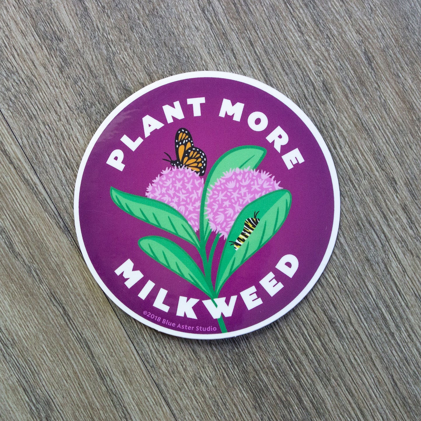 A round vinyl sticker with an illustration of a common milkweed plant in the center and the words Plant More Milkweed around it.