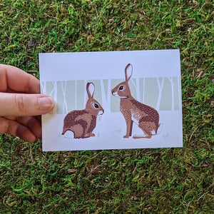 A hand holding a greeting card with an illustration of two cottontail rabbits on it.