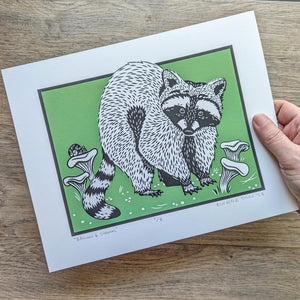 The 8x10 raccoon and shrooms screen print with the green background being held in a hand to show scale.