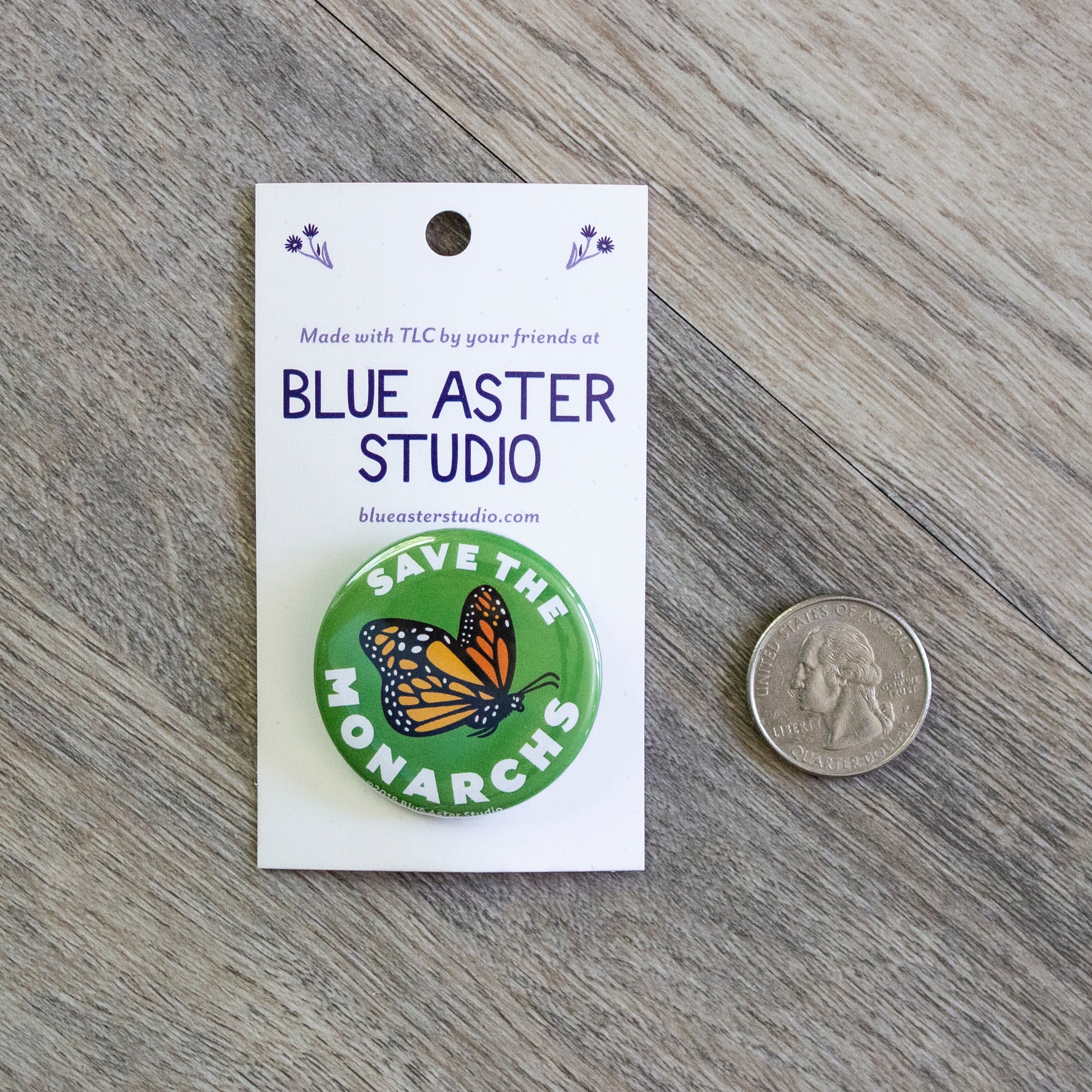 A 1.5 inch green pinback button with an illustration of a monarch butterfly in flight and the words Save The Monarchs. A US quarter is next to the button for scale.