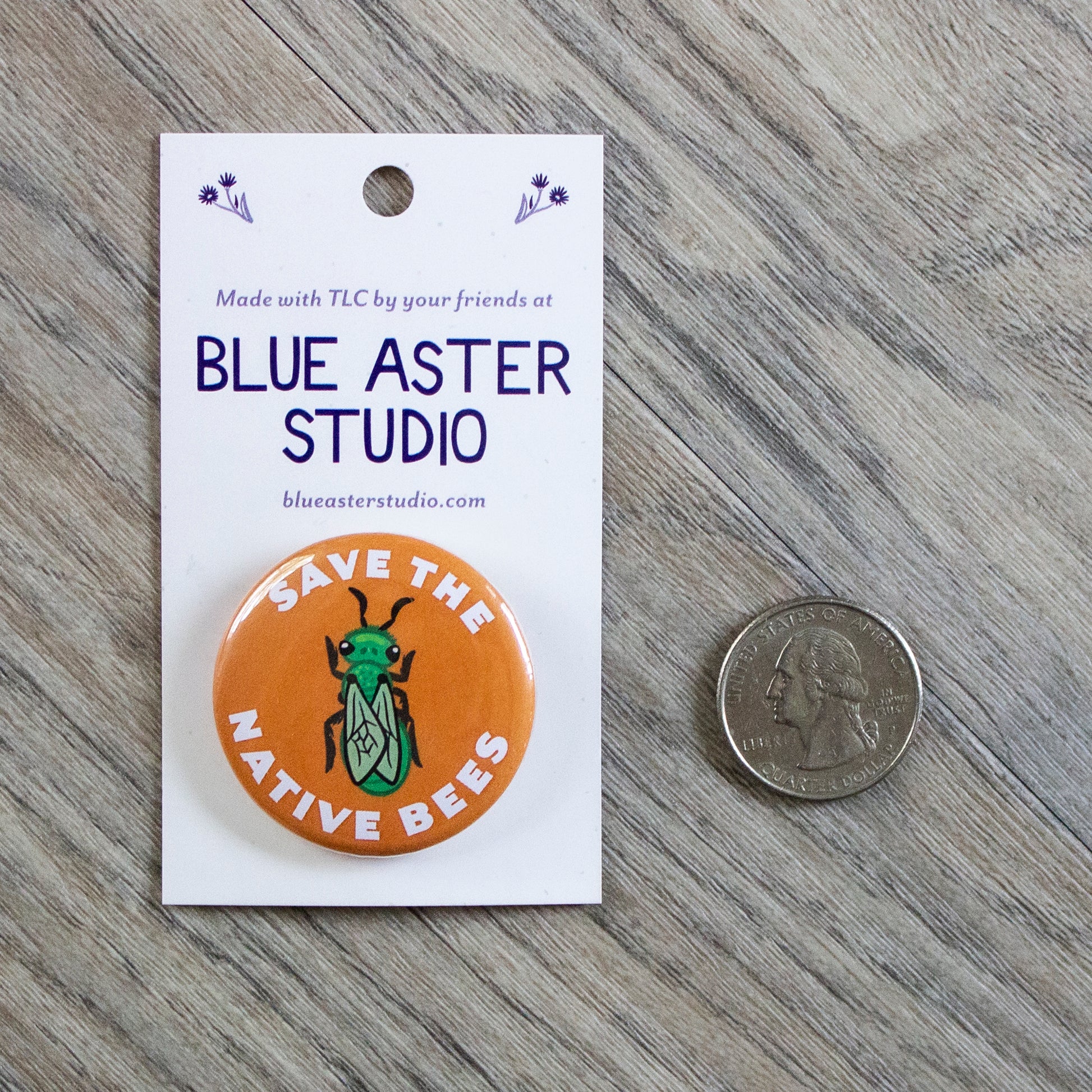 Save the Native Bees pinback button on grainy wood background. Button art is a green sweat bee on an orange background. A US quarter is next to the button for scale.