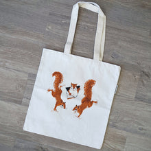 Load image into Gallery viewer, A squirrel tote bag featuring three illustrations of squirrels climbing and peeking out of the tote. The bag is made of a durable organic cotten fabric.
