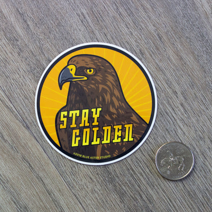 The golden eagle Stay Golden sticker sitting next to a USD quarter to show scale.