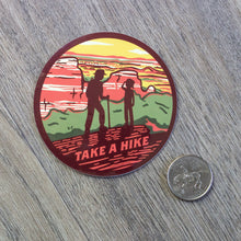 Load image into Gallery viewer, The round Take A Hike vinyl sticker sitting next to a USD quarter for scale.