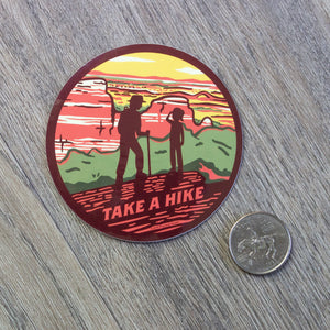 The round Take A Hike vinyl sticker sitting next to a USD quarter for scale.