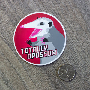 The opossum vinyl sticker sitting next to a USD quarter to show scale.