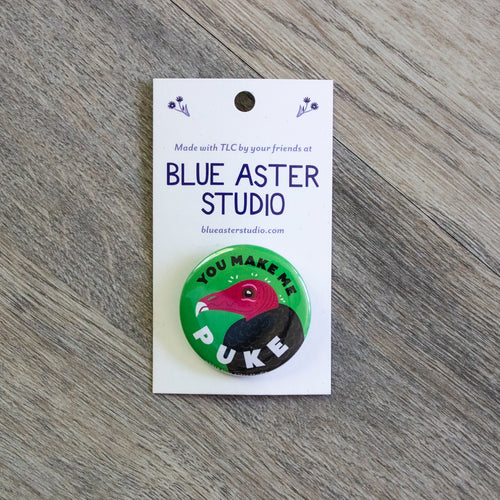 A 1.5 inch green pinback button with an illustration of a turkey vulture and the words You Make Me Puke.