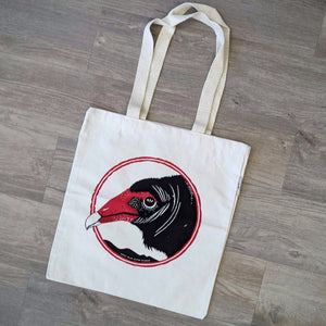 An organic cotton turkey vulture tote bag. The bag has a turkey vulture face screen printed on it in black and red.