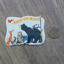 Load image into Gallery viewer, A vinyl sticker with an illustration of a fox, rabbit, turtle, owl, raccoon, bear, opossum, snake, and bird holding a flag that reads &quot;Keep Us Wild&quot; sitting next to a USD quarter for scale.