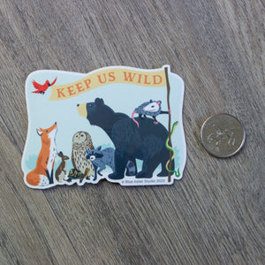 A vinyl sticker with an illustration of a fox, rabbit, turtle, owl, raccoon, bear, opossum, snake, and bird holding a flag that reads "Keep Us Wild" sitting next to a USD quarter for scale.
