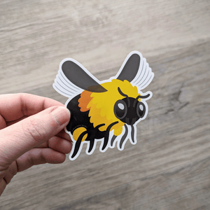 A hand holding a bumblebee vinyl sticker.
