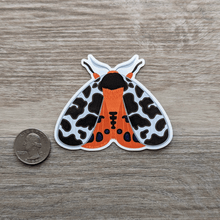 Load image into Gallery viewer, The vinyl sticker of a garden tiger moth next to a USD quarter to show scale.