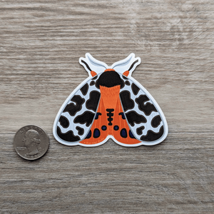 The vinyl sticker of a garden tiger moth next to a USD quarter to show scale.